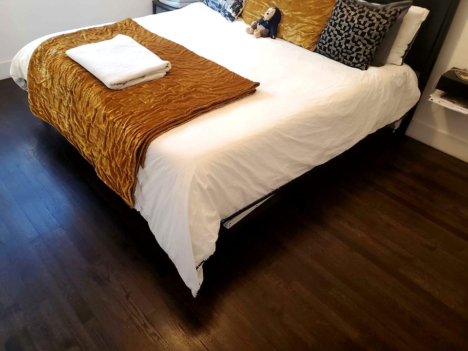 A freshly made bed with a folded towel and clean hardwood floor